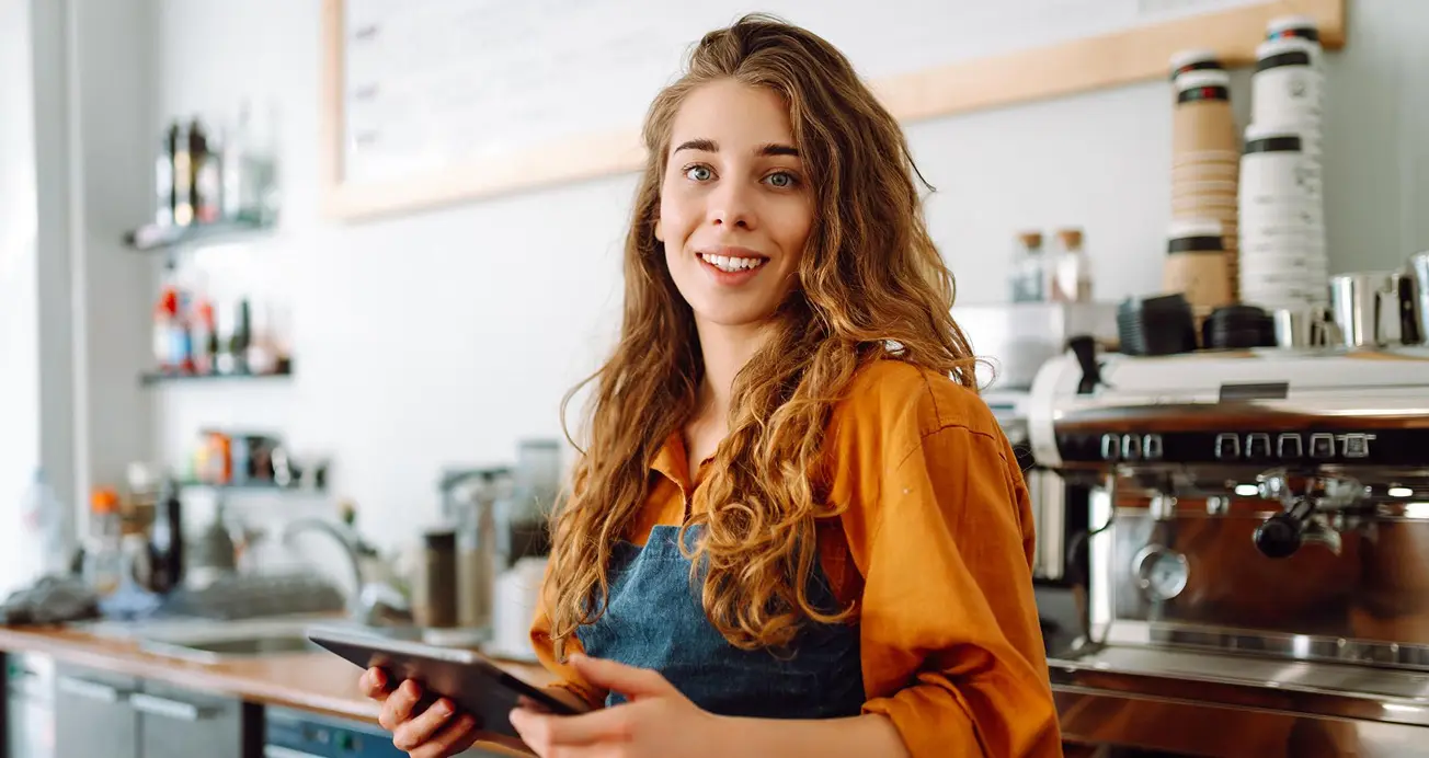 A smiling cafe owner holding a tablet behind the counter